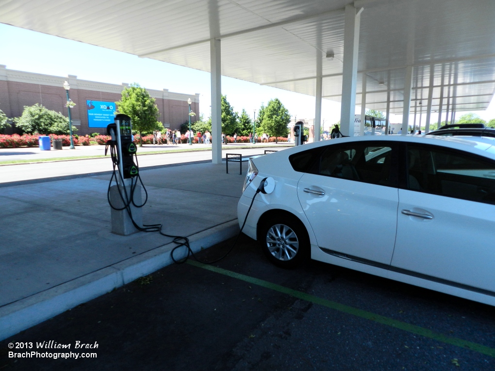 The white car is plugged into the charging station and charging up while the owner is either inside the park or inside Chocolate World.