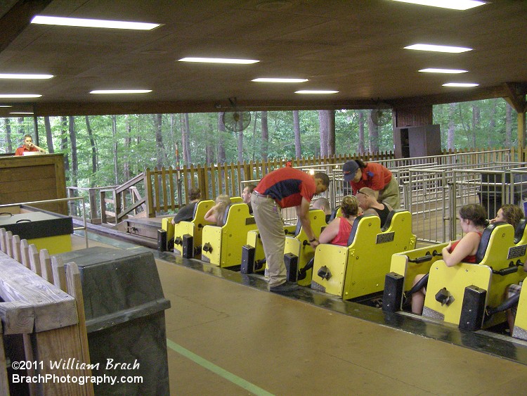 Ride Ops checking lapbars and seatbelts on the yellow train inside the station.