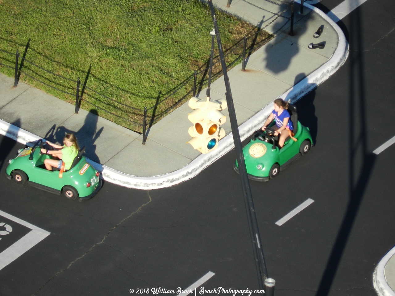 Two green cars being driven by kids.