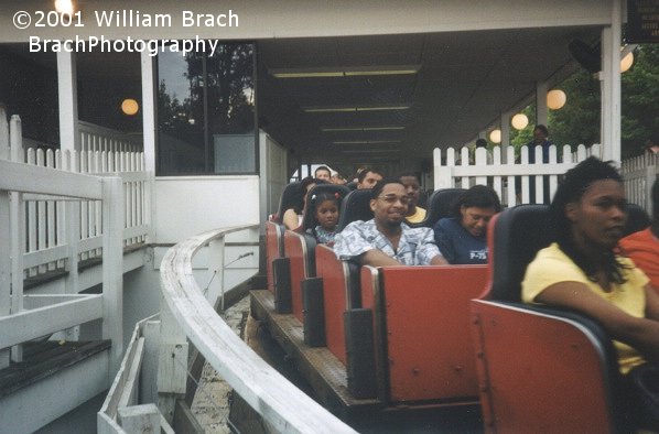 Forward facing red train departs the station enroute to the lift hill.