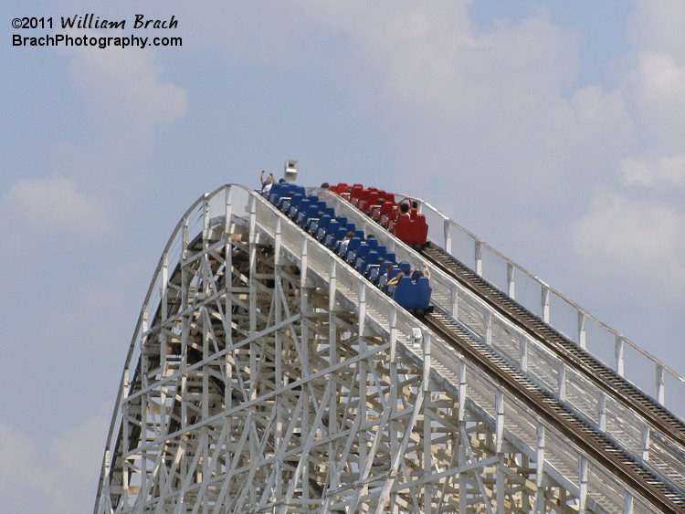 Red train is already going over the hill whiel the blue train has yet to crest the top of the lift hill.