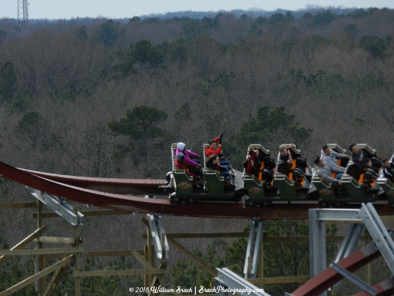 Green train has left the lift hill and is gaining speed to go down the barrel roll drop.