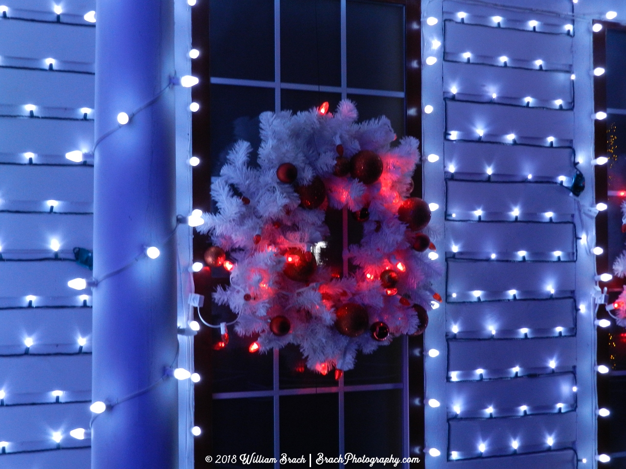 Very white wreath with red lights and bulbs on it.