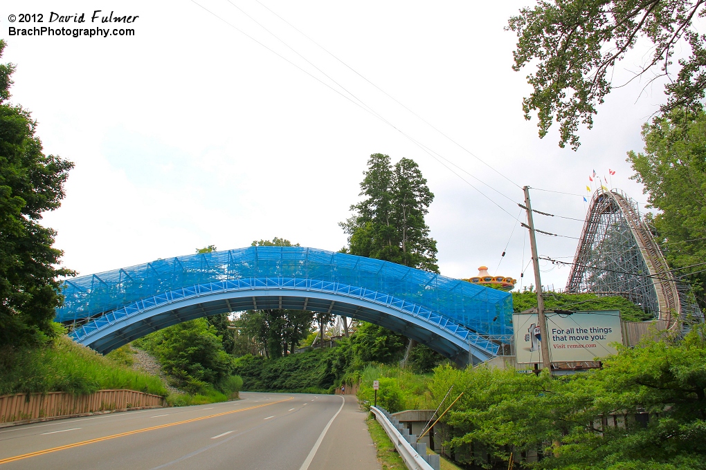 Overview of the lift hill, first drop and coaster bridge on busy road.